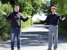 two men standing next to each other on a road with trees in the background