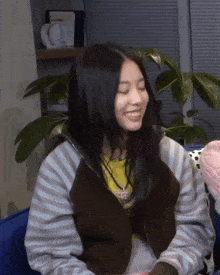 a woman wearing a striped jacket and a yellow shirt smiles with her eyes closed