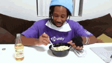 a man wearing a purple shirt that says unity is eating a bowl of food