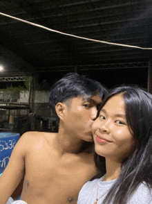 a shirtless man kisses a woman on the cheek in front of a sign that says 5636