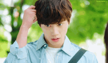 a young man in a blue shirt is scratching his head with his hand