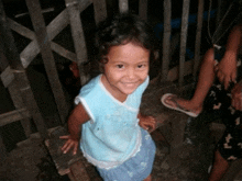 a little girl in a blue shirt and skirt smiles for the camera
