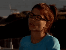 a woman wearing glasses and a blue shirt making a funny face