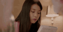 a woman is reading a book in front of a lamp .