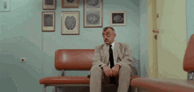 a man in a suit and tie sits on a couch in front of a wall with brain drawings on it