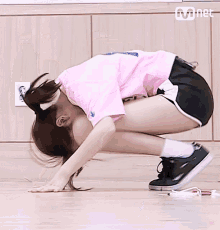 a woman in a pink shirt and black shorts is kneeling down on the floor .