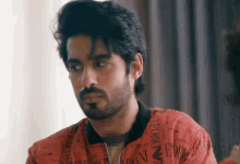 a man with a beard is wearing a red emporio armani shirt