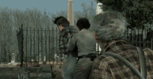 a man in a plaid shirt is walking with two other men in a cemetery