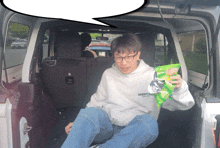 a man in a hoodie that says essentials sits in the back of a car