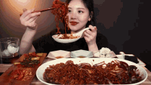 a woman eating noodles with chopsticks and a spoon