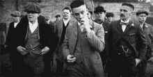 a black and white photo of a group of men in suits and hats walking down a street .