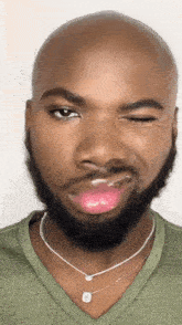 a bald man with a beard wearing a green shirt and a silver necklace is making a funny face .
