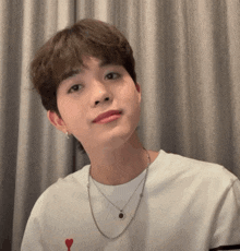 a young man wearing a white shirt and a silver necklace