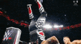 a wrestler is doing a handstand in the air while another wrestler looks on .