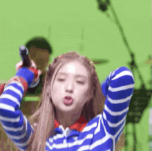 a woman in a blue and white striped shirt is holding a microphone in her hand .
