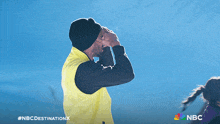a man wearing a yellow vest and a black hat is clapping his hands in front of a blue sky