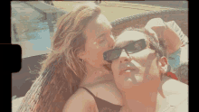 a woman kissing a man on the cheek while he wears sunglasses