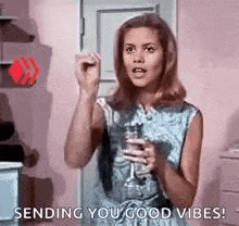 a woman is standing in a room holding a glass of wine and sending you good vibes .