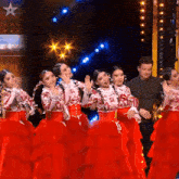 a group of women in red dresses are dancing on a stage with a man standing behind them