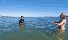 a woman in a bikini is standing in the water next to a child in a wet suit