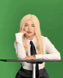 a woman in a white shirt and black tie leans on a table with her hand on her chin