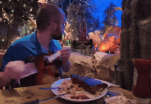 a man sits at a table with a plate of food in front of a sign that says " treasurelands "