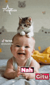 a baby laying on a bed with a cat on top of his head