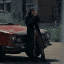 a woman standing in front of a red car taking a picture