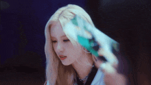 a woman with blonde hair is holding a green object in her hand and looking at the camera .