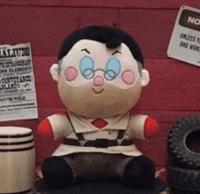 a stuffed toy of a man with glasses is sitting on a table next to a tire .