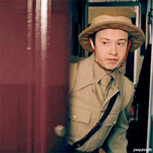 a man wearing a safari hat is standing in front of a red door ..