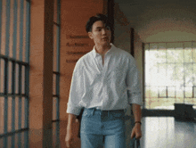 a man in a white shirt and blue jeans walks down a hallway