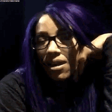 a woman with purple hair and glasses is wearing a black jacket .