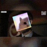 a man in a suit has a picture of a cat on his face in front of a bbc logo