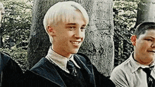 a young man with blonde hair is smiling while standing next to a group of young men .