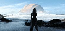 a silhouette of a woman standing on a beach with a mountain in the background