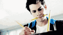 a young man is biting a pencil in his mouth while writing on a piece of paper .