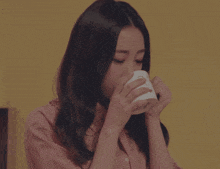 a woman in a plaid shirt is drinking from a white mug