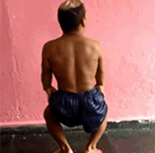 a shirtless man in blue shorts squatting on a pink surface .