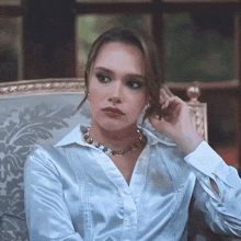a woman in a white shirt and gold necklace is sitting on a chair