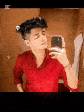 a young man in a red shirt is taking a selfie with his cell phone .