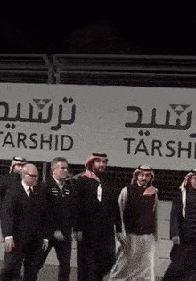 a group of men are standing in front of a sign that says tarshid