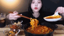 a woman is eating a bowl of soup with chopsticks