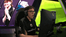 a man wearing headphones and a shirt that says heretic is sitting in front of a computer