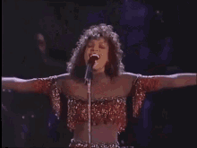 a woman is singing into a microphone with her arms outstretched on a stage .