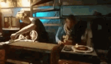 a couple of people are sitting at a table with a pizza box on it .