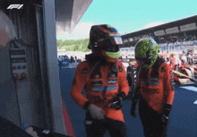 a man wearing a green helmet talks to another man in an orange suit