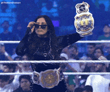a woman in a wrestling ring holding a championship belt and wearing sunglasses
