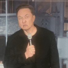 a man in a black jacket is holding a microphone and making an angry face