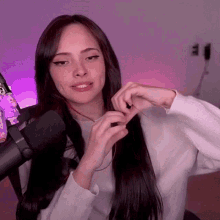 a woman with long dark hair is sitting in front of a microphone and making a heart shape with her hands .